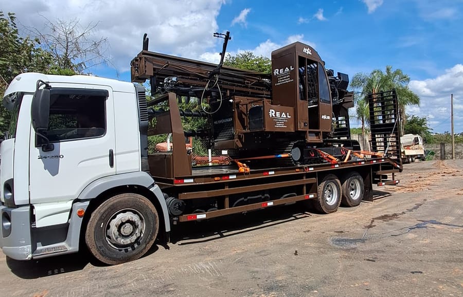 Foto do equipamento: Caminhão prancha carregado com perfuratriz sobre esteiras para movimentação do equipamento.